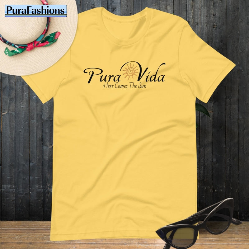"Brighten up your day with our sunny yellow T-shirt, adorned with the uplifting message 'Pura Vida' and a radiant sun graphic. Embrace positivity and optimism with every wear. Find it now at PuraFashions.com."