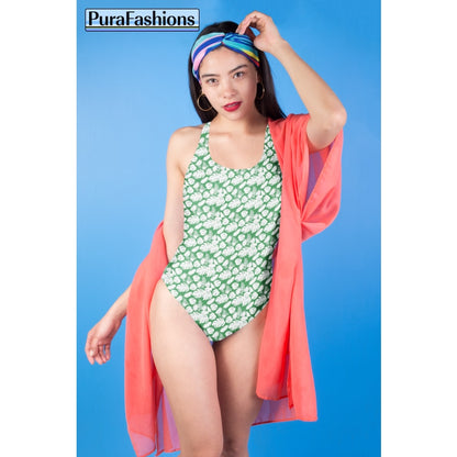 "Tropical allure: A woman stands against a vibrant blue sky, showcasing a one-piece swimsuit from PuraFashions.com adorned with a lush tropical leaves pattern on a serene sea green background, embodying the essence of paradise."