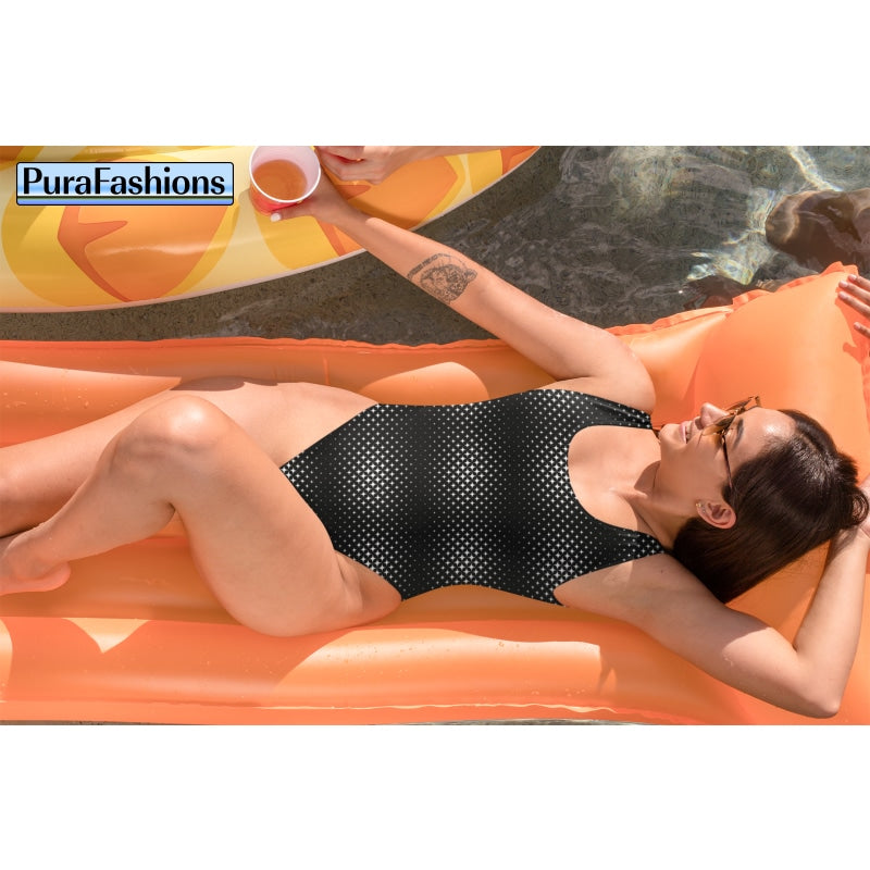 "Beachside relaxation: A woman lounges gracefully on the sandy shore in a black one-piece swimsuit with a delicate white star pattern from PuraFashions.com, embodying both comfort and style amidst the tranquil beauty of the beach."