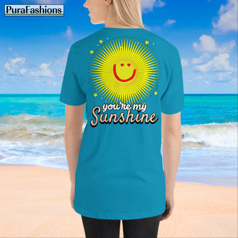 "Back view of a woman wearing an aqua T-shirt with a large happy face sun and a few stars, along with the text 'You're My Sunshine'. The T-shirt has a small happy face sun and stars on the front as well. Available at PuraFashions.com."