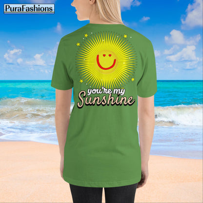 "Back view of a woman wearing an leaf green T-shirt with a large happy face sun and a few stars, along with the text 'You're My Sunshine'. The T-shirt has a small happy face sun and stars on the front as well. Available at PuraFashions.com."