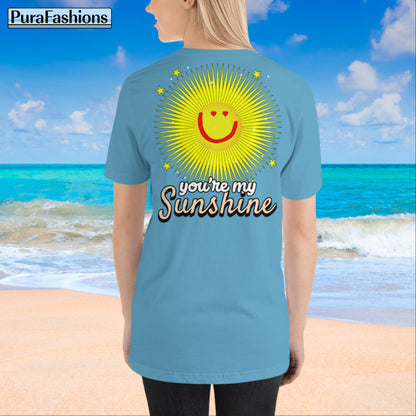 "Back view of a woman wearing an ocean blue T-shirt with a large happy face sun and a few stars, along with the text 'You're My Sunshine'. The T-shirt has a small happy face sun and stars on the front as well. Available at PuraFashions.com."