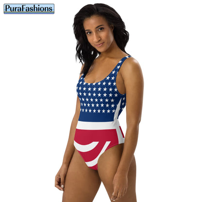 "Angled Elegance: Elevate your beach style with our USA Flag Print One-Piece Swimsuit, available at PuraFashions.com. This captivating image captures the essence of grace and patriotism as a woman showcases the sleek design against a pristine white background. The striking USA flag print adds a bold touch to your swimwear collection, while the impeccable fit ensures comfort and confidence. Make a statement with every step, embodying the spirit of freedom and fashion."